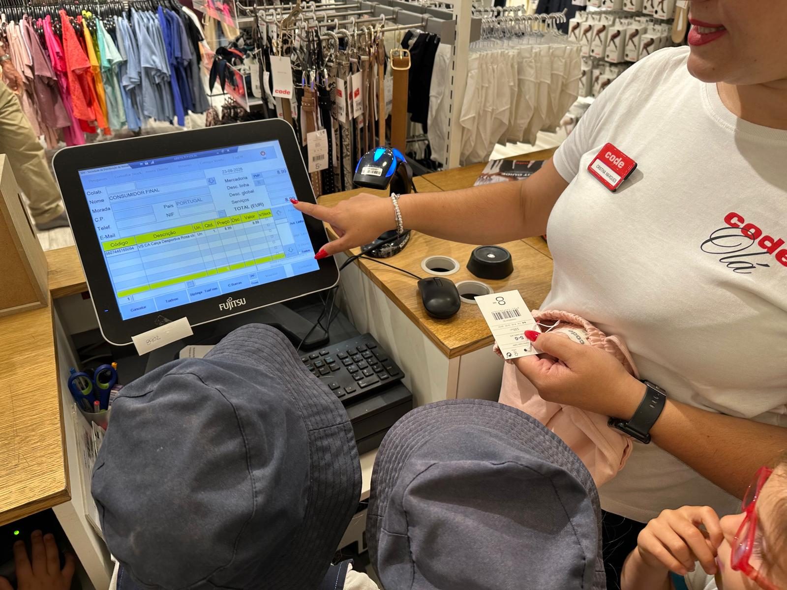 Crianças junto ao balcão de uma loja de roupa, a observar a caixa