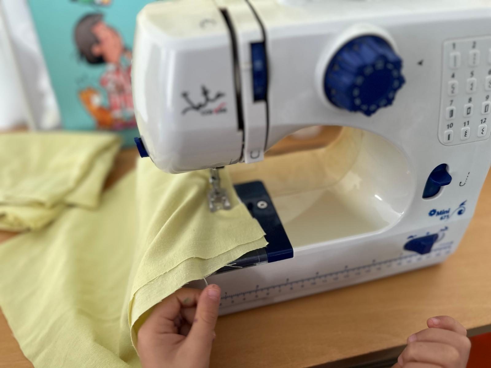 Mãos de uma criança a guiar um tecido numa máquina de costura