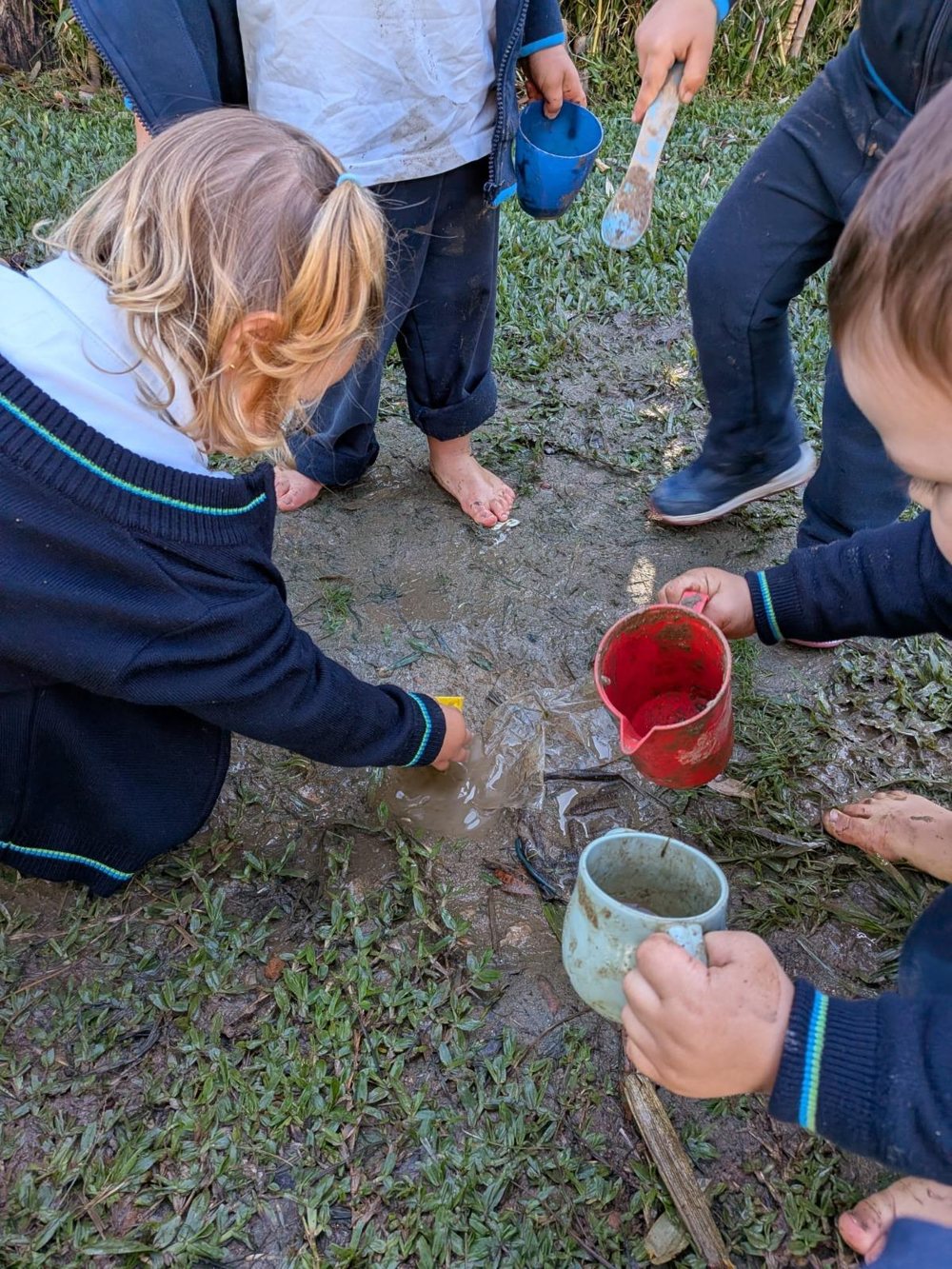Duas crianças a explorar a lama com as mãos e com recipientes