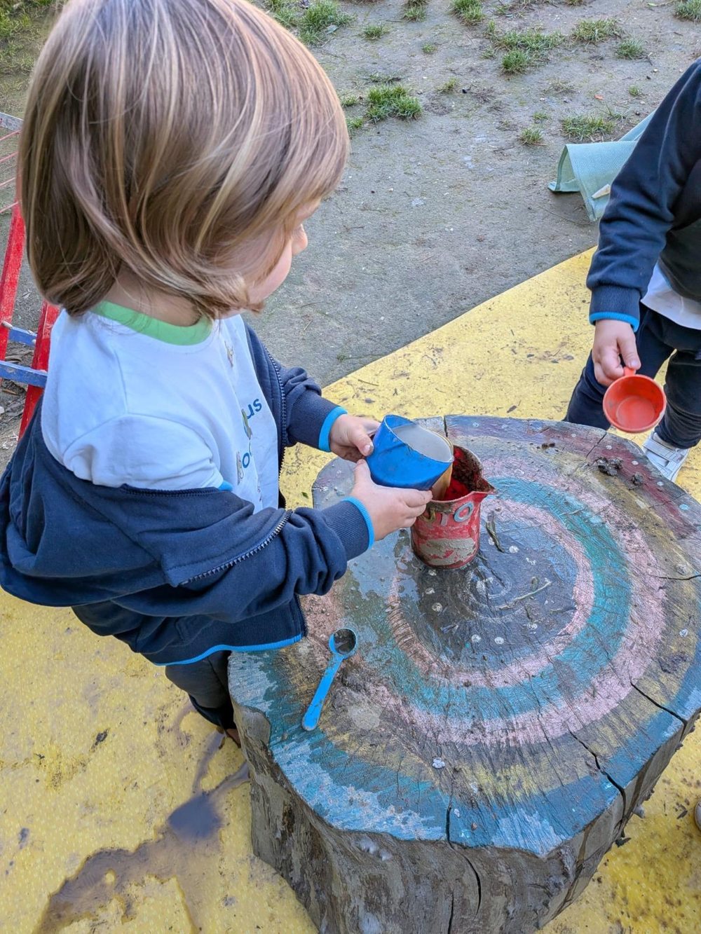 Criança a transferir água entre recipientes sobre um tronco pintado