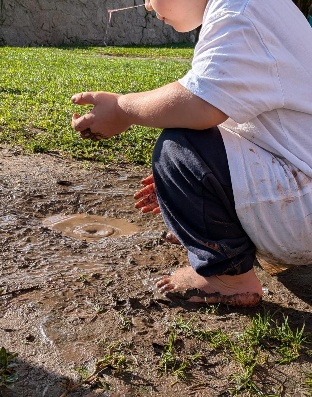 Criança agachada junto a uma poça de lama, com uma ondulação na água
