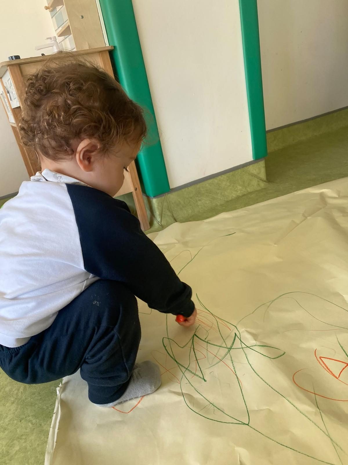 Criança a desenhar num papel de cenário no chão